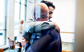 man warmly embraces another man in a hallway, expressing a heartfelt connection and friendship.